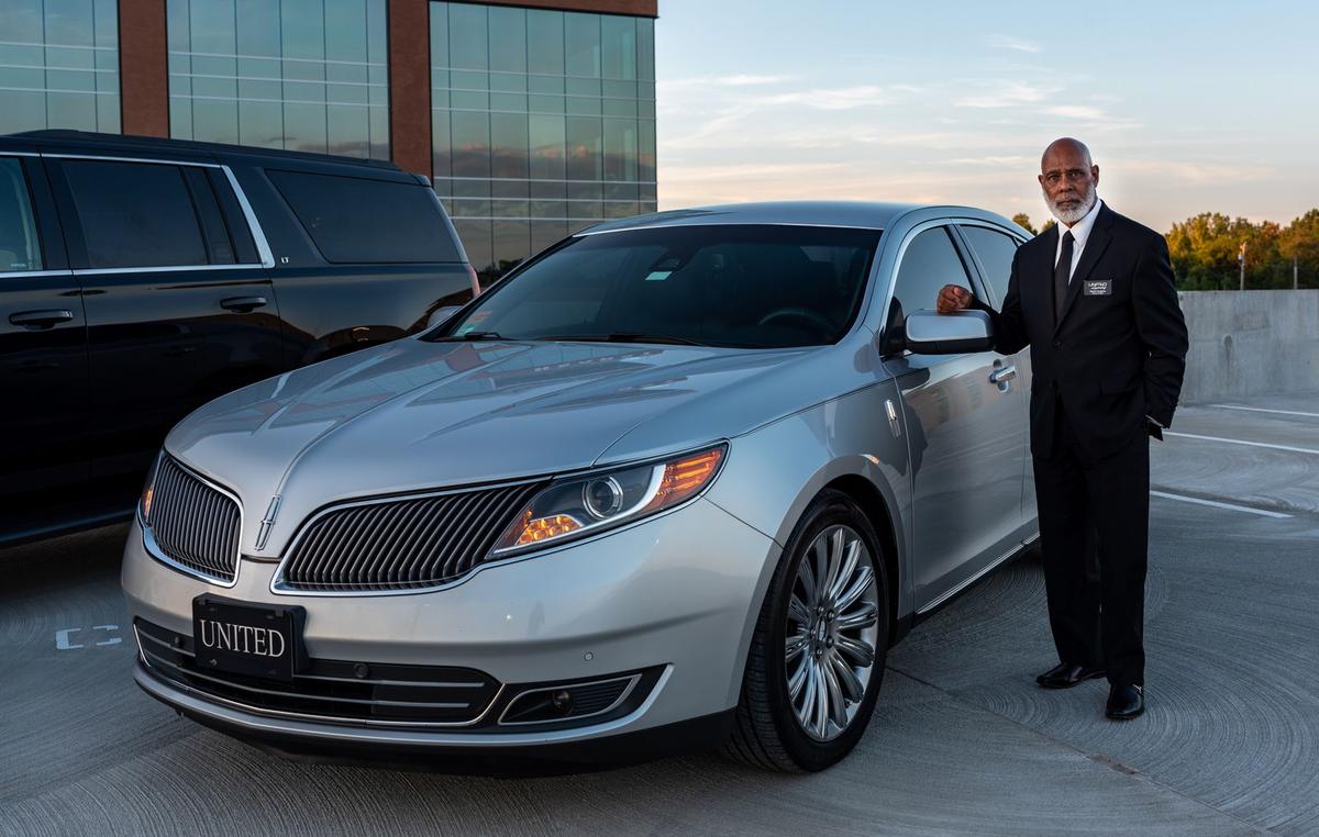 Professional chauffeur standing beside a luxury car
